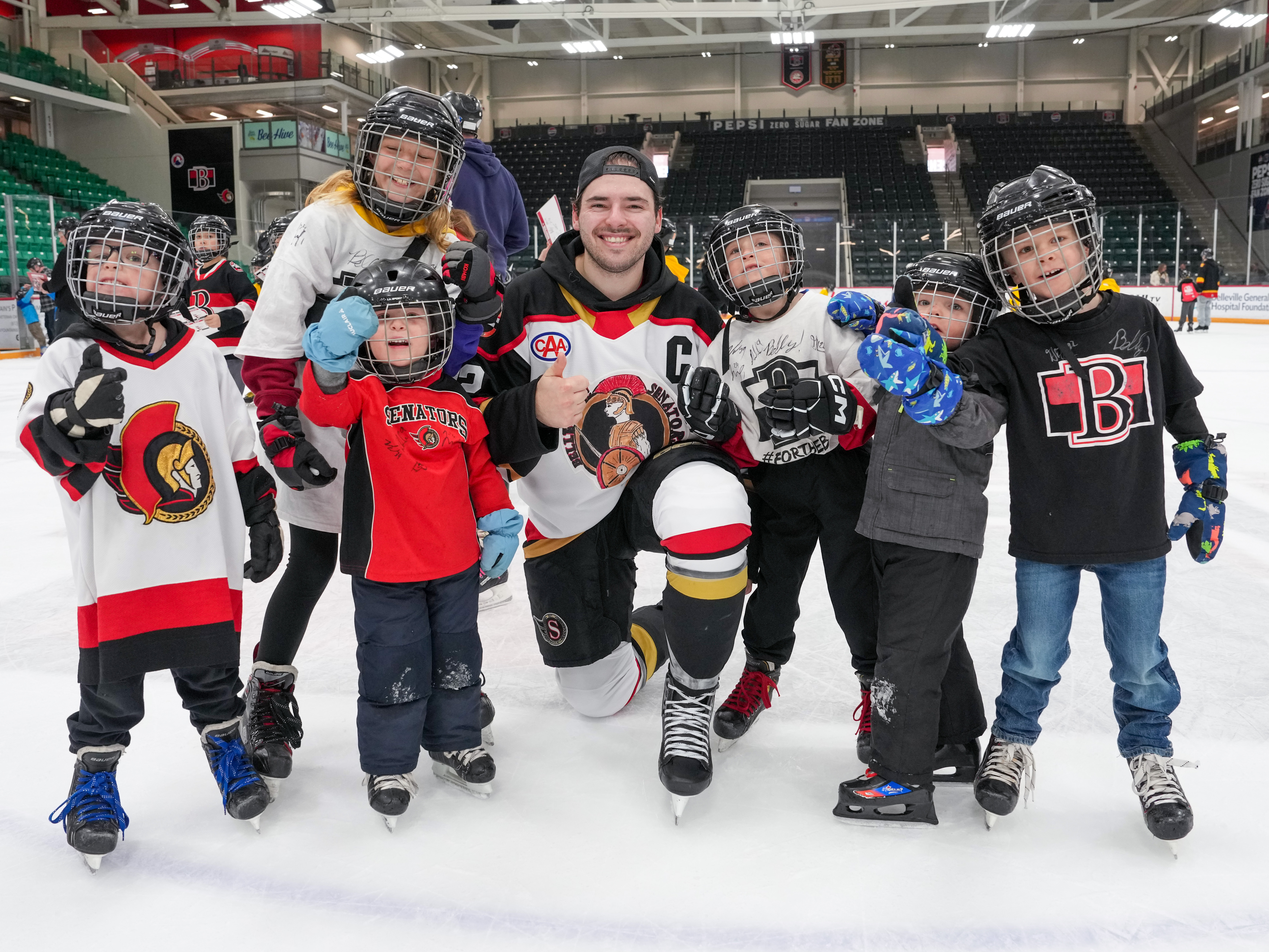 A hockey player poses for a photo with some young fans during a post game skate.